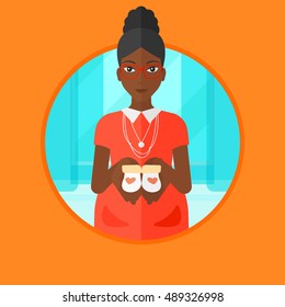 An african-american young pregnant woman holding baby booties in hands. Smiling pregnant woman holding baby booties on the belly. Vector flat design illustration in the circle isolated on background.