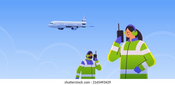 airport workers marshallers communicating over walkie-talkie with air traffic control while airplane flying in sky