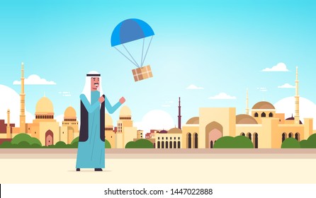 Arab-Mann-Fang-Paket-Box herunterfallen mit Fallschirm-Versandpaket Luftpost Express Postzustellung Konzept nabawi Moschee Gebäude muslim Stadtlandschaft Hintergrund volle Länge horizontale