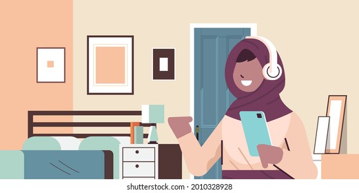 arabic schoolgirl using smartphone and listening to music in headphones arab girl with gadget relaxing at home