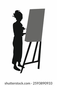 Artist woman is painting on a canvas. She is wearing black clothes and has her hair in a bun. The painting is on a wooden easel
