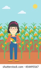 An asian female farmer holding a corn cob. Young farmer standing on the background of corn field. Vector flat design illustration. Vertical layout.