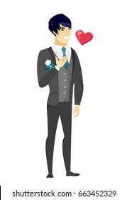 Asian groom in a wedding suit holding hand on chest. Full length of young happy groom with hand on his chest and heart flying nearby. Vector flat design illustration isolated on white background.