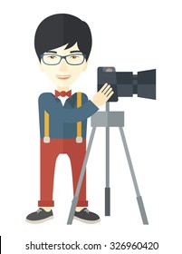 An Asian photographer in glasses standing with camera on a tripod vector flat design illustration isolated on white background. Vertical layout.