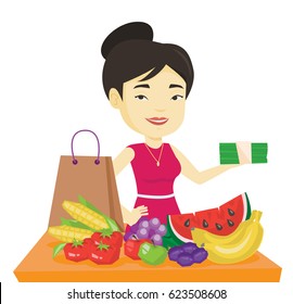 Asian shopper standing at the table with grocery purchases. Young shopper holding money in hand in front of table with grocery purchases. Vector flat design illustration isolated on white background.