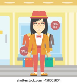 An asian woman holding shopping bags on the background of boutique window with dressed mannequins. Happy young woman carrying shopping bags. Vector flat design illustration. Square layout.