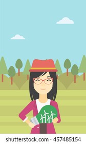 An asian woman standing on the background of green forest and holding in hands a big light bulb with small wind turbines inside. Green energy concept. Vector flat design illustration. Vertical layout.