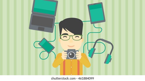An asian young man taking photo with digital camera. Man surrounded with gadgets. Man using many electronic gadgets. Vector flat design illustration. Horizontal layout.