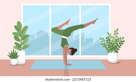 An athletic woman performs a handstand of yoga or gymnastics in a room with flowers and a large window overlooking the city. The concept of a healthy and active lifestyle, sports.