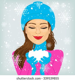 attractive brunette woman with eyes closed and smiling in blue winter hat and scarf holding snow