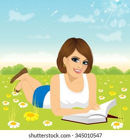 attractive brunette woman lying down on grass reading book in the peaceful park