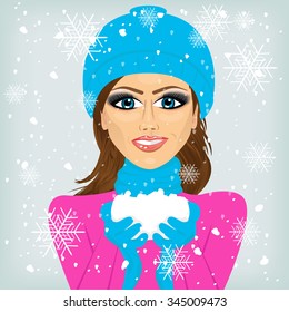 attractive brunette woman smiling in blue winter hat and scarf holding snow