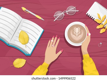 Autumn flat lay background with workplace in a cafe. Women's hands holding a Cup of cappuccino. Burgundy wooden background with yellow autumn leaves. Book, notebook, eye glasses.
