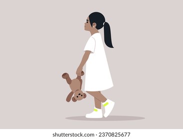 A baby girl in a white dress playfully holding a teddy bear upside down by its paw