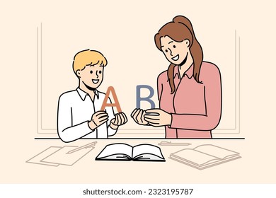 Back to school concept with boy learning alphabet along with elementary school teacher standing near table with books. Woman teaches child read or spell correctly, wanting give son quality education