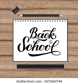 Back to school lettering hand written in a notebook. Wooden texture background and stationery. Vector template for advertising poster, logo design, banner, flyer, sign, greeting card, invitation, etc.