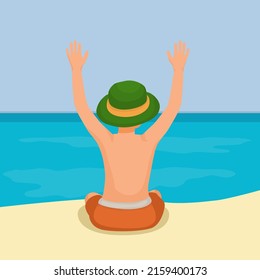 back view of cute little boy wear hat sitting on sand raising hand having fun on the beach enjoying summertime