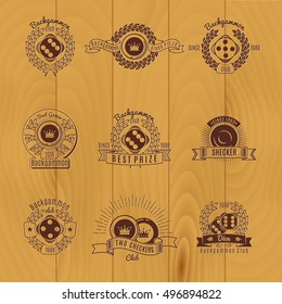 Backgammon monochrome emblems with components of game laurel leaves and ribbons on wooden background isolated vector illustration  
