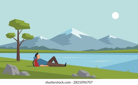 Backpacker relaxing on green grass field by a calm lake while looking at majestic snow-covered mountains in distance.