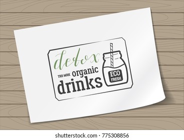 Badge in Frame Detox Organic Drinks with Hand Drawn Lettering and Jar Icon on A4 Sheet Paper on Wooden Background. Green Emblem Vector Illustration.