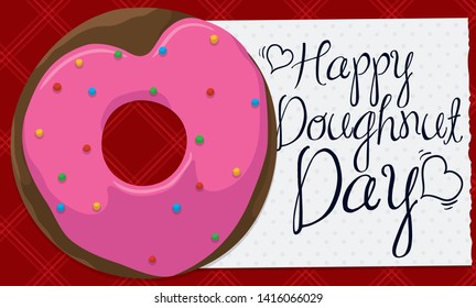 Banner with a delicious donut with heart shape glaze, sprinkles and a greeting message written in a napkin, all over squared tablecloth ready to celebrate Doughnut Day.