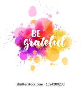 Be grateful - handwritten modern calligraphy inspirational lettering on abstract multicolored watercolor splash background. 