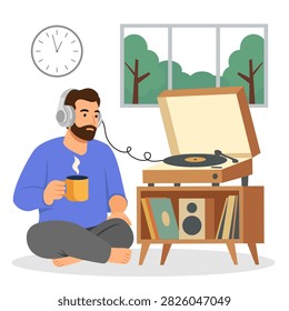 A bearded man sits cross-legged on the floor listening to music on a turntable. He wears over-ear headphones while holding a steaming mug. The cozy room features a wooden console, wall clock, and window. Perfect for music lifestyle concepts.