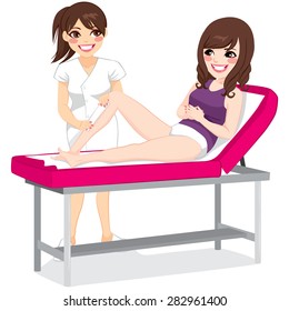 Beautiful beautician waxing young woman legs lying on spa bed