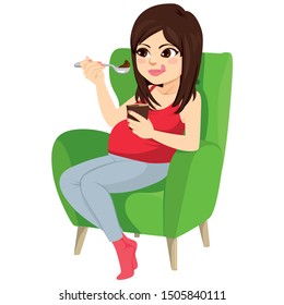 Beautiful brunette pregnant woman holding spoon eating chocolate ice cream sitting on green armchair craving concept