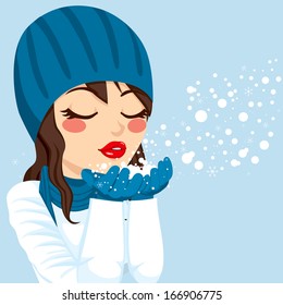 Beautiful brunette woman with warm blue winter hat and scarf gently blowing snow from her hands showing Christmas magic concept