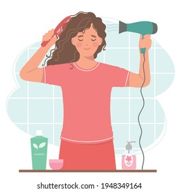 Beautiful curly-haired woman dries her hair with a hair dryer. She's holding a hair dryer and a hairbrush.