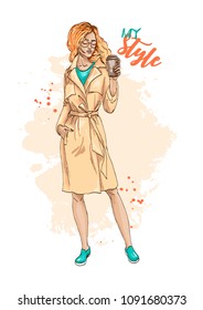 Beautiful fashionable girl with red hair in glasses, holding a glass of coffee. Stylish young woman posing. Fashion illustration. Vector. Hand drawn sketch.