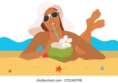 Beautiful girl in glasses with a hat and a coconut in her hands sunbathes on a beach by the sea