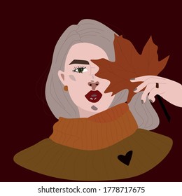 A beautiful girl with light hair and warm autumn clothes holds orange autumn leaf leaning against her face in her hand