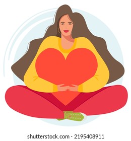 A beautiful and happy woman embraces a big heart with love. The girl sits in the lotus position with long hair and enjoys life. Positive thinking and awareness.