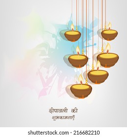 Beautiful illuminated hanging oil lit lamps on colorful abstract background with wishes in Hindi text for Diwali festival celebrations. 