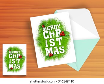 Beautiful ornaments decorated greeting card design with envelope on wooden background for Merry Christmas celebration.