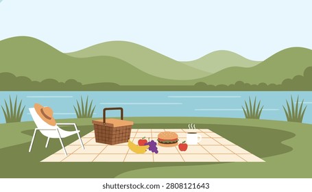 Beautiful summer picnic setup on a blanket by the lake with a wicker basket, fresh fruits, hamburger, coffee cup, and hills behind.