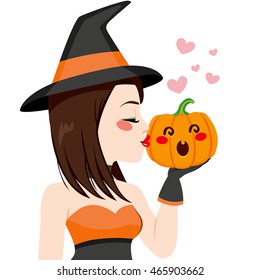 Beautiful young brunette witch kissing pumpkin on Halloween
