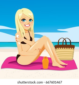 Beautiful young happy blonde woman applying suntan cream on her arms sitting in pink towel at beach sunbathing