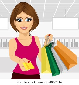 beautiful young woman holding shopping bags and giving a credit card in the supermarket