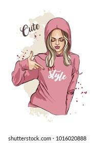 Beautiful young woman in sports sweatshirt. Pointing at the inscription on the chest. Casual style. Fashion model posing. Vector illustration of fashion. Hand drawn sketch.