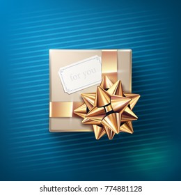 The beige gift box with the white greeting card and glittering golden bow with ribbons isolated on blue background. Vector realistic decoration element for holiday design. Top view