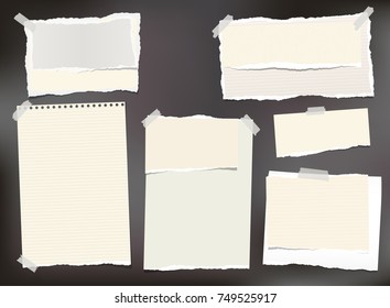 Beige ripped paper, notebook sheets, note paper for text or message stuck with sticky tape on black background.