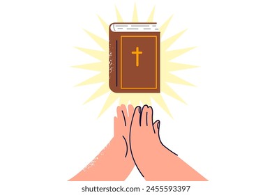 Bible with rays of light near hands of praying man who professes christian religion and reads catholic or orthodox literature. Bible book with crucifix on cover allows believer to become closer to god