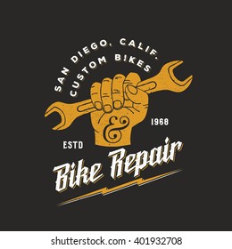 Bike Repair Abstract Vintage Vector Sign, Label Or Logo Template. Fist Holding Wrench With Retro Typography And Shabby Textures. On Dark Background.