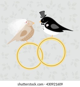 Birds in costumes of the bride and groom sit at the wedding rings