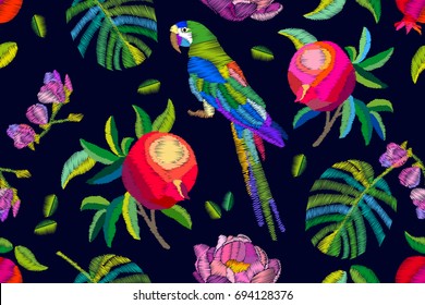 Birds in the pomegranate garden. Seamless vector pattern with parrot, fruits, palm leaves and flowers. Embroidered texture. Vintage textile collection.