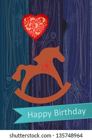 Birthday Greeting card with a toy wooden rocking horse and red heart shaped balloon on a decorative blue wooden background with a turquoise banner or ribbon bearing the words, Happy Birthday