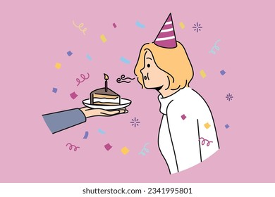 Birthday woman blows out candle on piece of cake celebrating anniversary and making cherished wish. Girl in birthday hat stands among confetti celebrating day of angel and dreaming about future